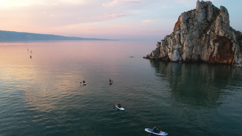 Sunset over Lake Baikal in summer. Tourists swim on sap boards in the bay of the lake. Active water recreation.