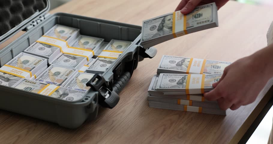 Person pack 100 dollar bills into briefcase. Bribes of financial success and wealth