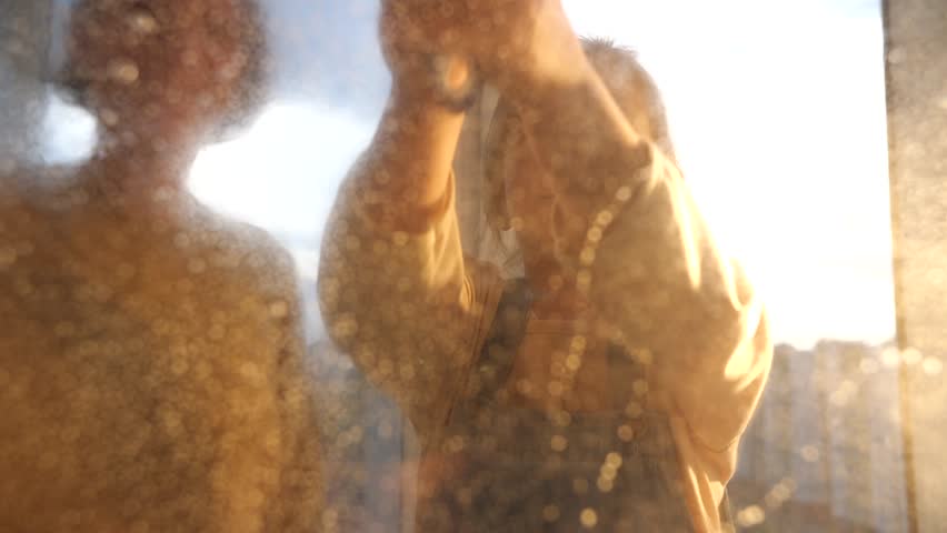 A young woman and a little girl are washing a window in their apartment