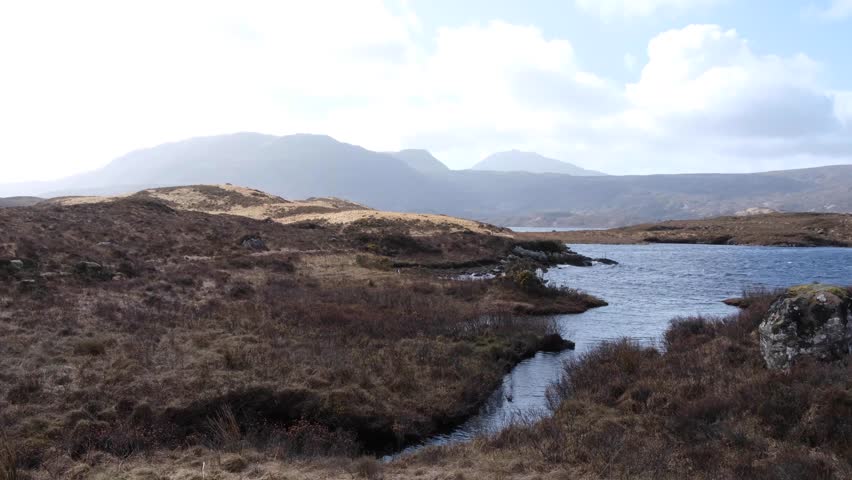 Slow pan of Lewisian gneiss landscape overlooking Loch Inver water, islands with trees, and tussock grasses in the highlands of Scotland UK