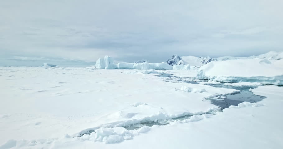 Arctic snow covered wild nature winter landscape. Aerial fly over polar ice ocean, frozen icebergs and mountains towering coastline in background. Antarctica travel and exploration. Low angle shot