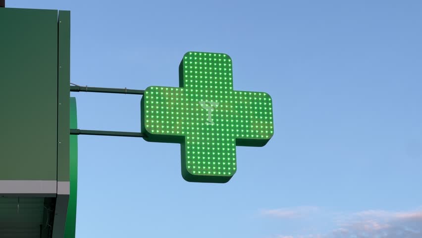 Green Cross Pharmacy Beacon Illuminates the Heart of an Urban Oasis, Shining Beneath Blue Skies