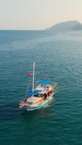 Aerial view of a tourist cruise boat near Cirali beach at Mediterranean sea and mountain at sunset. Olympos and Cirali Beach In Antalya Province, Turkey. Drone footage