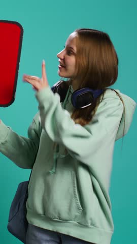 Vertical video Smiling woman holding red speech bubble sign of empty copy space for message. Joyous teenager presenting thought bubble cardboard used as promotion concept, isolated over studio