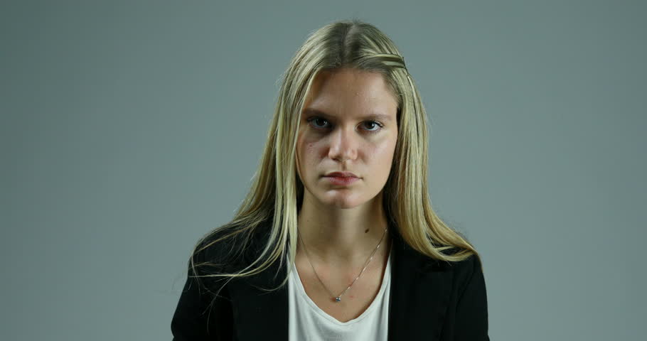 Slim blonde young woman in elegant black jacket listens, then smiles in agreement, against a neutral background
