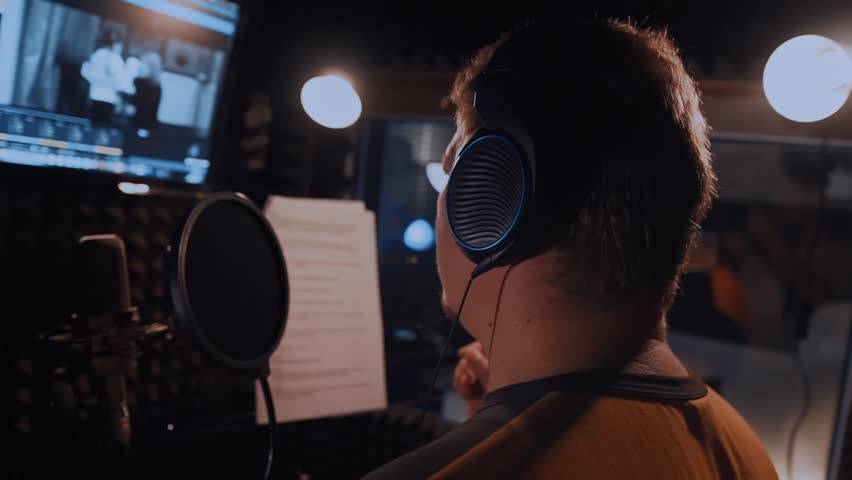 Professional voice actor recording audio book or podcast, portrait with microphone in recording studio, man creating audio advertising for radio or online sites, dubbing and dubbing in video