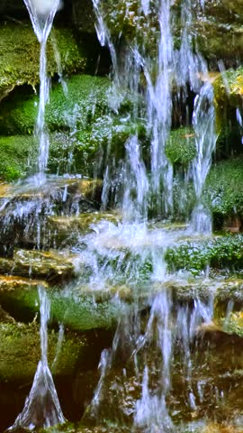 Decorative fountain of natural rocks and green moss, in the park on a summer day. Close-up.