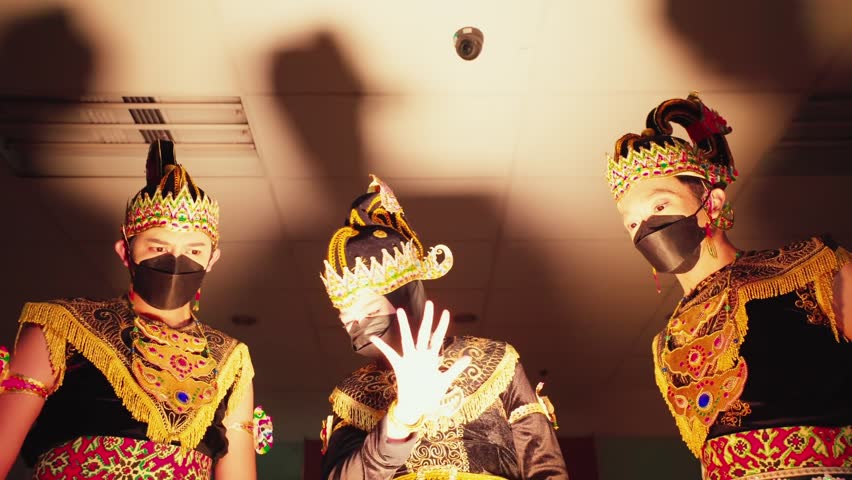 Three performers in traditional Javanese dance costumes with elaborate headdresses, captured in a dramatic stage lighting setting, showcasing cultural performing arts.