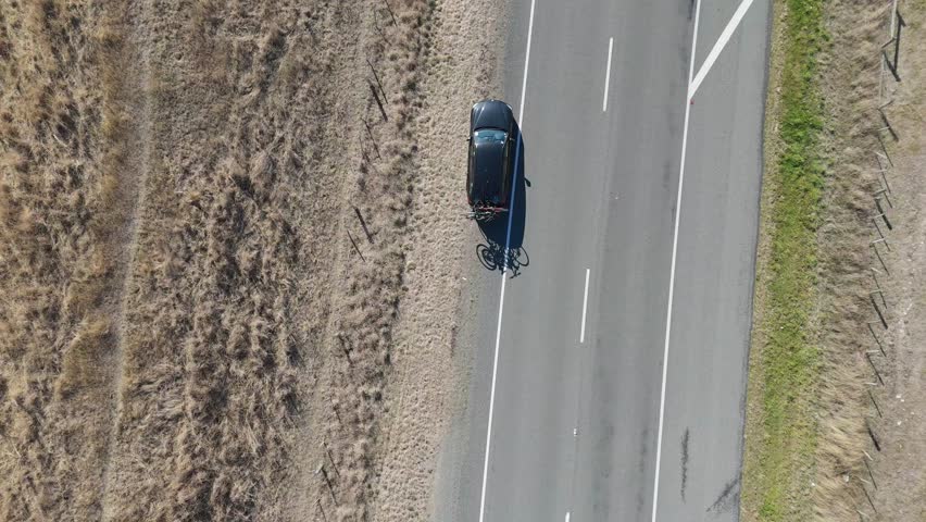 A car with bicycles on a trailer is driving along a road. Shooting from a drone