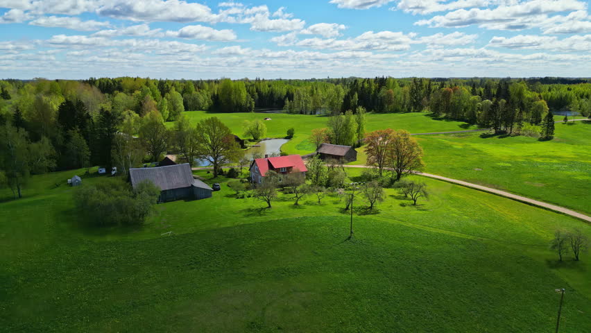 Beautiful small farmhouse with vast green meadow and forest in Latvia, aerial