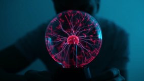 Silhouette of unrecognizable man looking at plasma ball with smooth magenta blue flames in dark room. Tesla lamp with high voltage lightning. Electromagnetic fields in glass globe, slow motion. - Powered by Shutterstock - Get 15% off with code: PIKWIZARD15