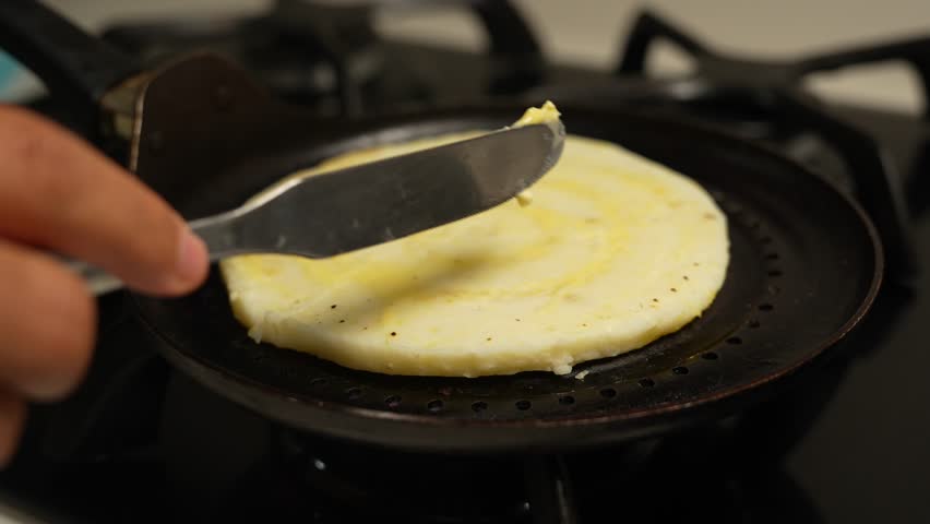 Cooking Colombian Traditional Breakfast. Adding Butter With Knife On Top of Arepa Grill. Gas Stove