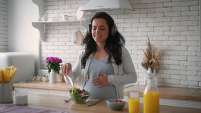 Happy fun active pregnant woman Caucasian girl enjoying pregnancy healthy female with belly mother in wireless headphones dancing listening music dance sing enjoy cooking salad eat tomatoes at kitchen - Powered by Shutterstock - Get 15% off with code: PIKWIZARD15