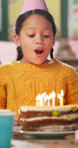 Girl, blow candles and birthday cake at kindergarten, happy and celebration with party hat, flame and food. Child, classroom and ideas for wish, dessert and excited for event at preschool academy