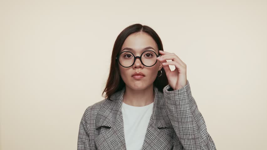 A young woman in a plaid jacket appears surprised as she lowers her eyeglasses.