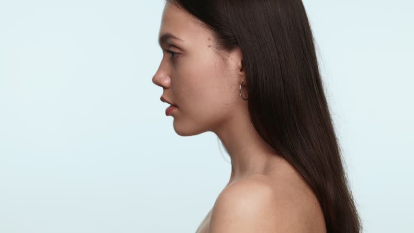 Portrait of a flirty young woman glancing playfully over her shoulder against a soft blue background.