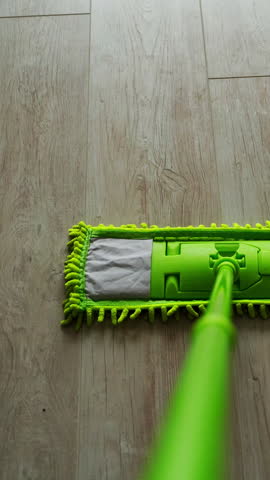 Cleaning floor with water and swab. Green mop moving on the parquet floor near the green bucket with water. Daily household routine. Hygiene concept. Vertical video