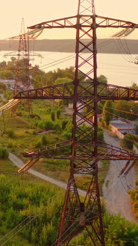 Transmission lines in the morning. High voltage electric lines near the river in summer. Tall electric towers at sunset. Aerial view. Slow motion. Vertical video