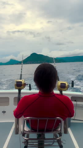 VERTICAL VIDEO. The back of a man fishing in a yacht during a beautiful sunny day. Recreation in the blue sea