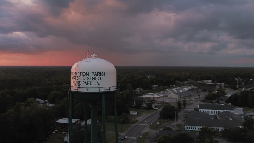 Aerial Panning Shot Of Text On Tall Water Storage Tank In Town Amidst Forest Trees Under Cloudy Sky During Sunset - Bayou Vista, Texas