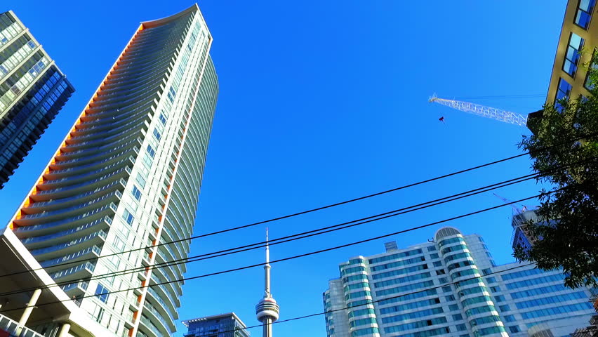 Panning Shot Of Cn Tower Amidst Tall Residential Buildings In City Under Clear Blue Sky On Sunny Day - Toronto, Canada