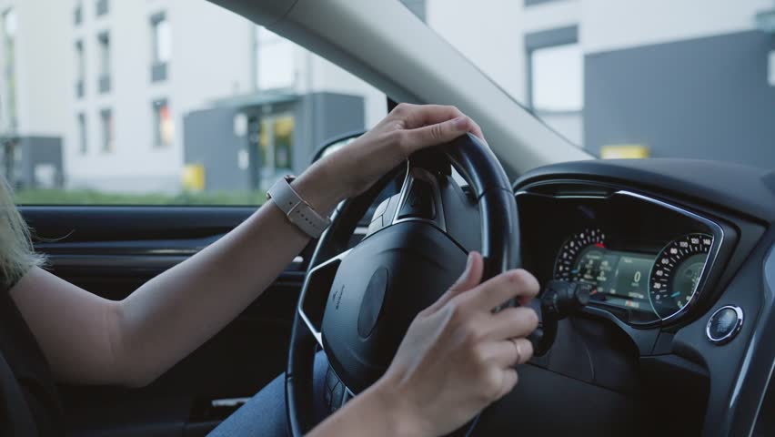 Female driver is parking car in parking lot in courtyard of house. Woman is driving car, moves in reverse and turning steering wheel