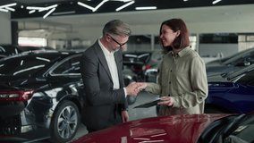A confident middle-aged man in glasses and a business suit a manager at a car dealership communicates with a brunette girl while signing a contract regarding a car in a modern car dealership - Powered by Shutterstock - Get 15% off with code: PIKWIZARD15
