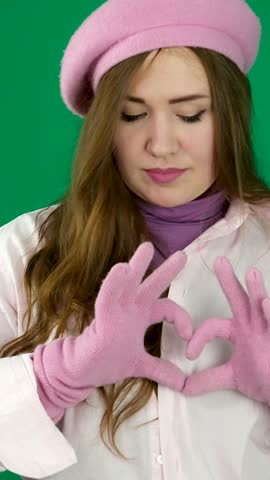 Beautiful girl, pink, beret, gloves, green background. She folds her hands into a heart shape and places them on her chest.