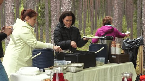Valmiera, Latvia - May 20, 2024 - A woman serving food outdoors in a forest setting, with a table full of dishes and beverages, preparing a meal for a group. Video Stok Editorial