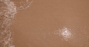 Close-up video of the breathtaking beauty of a sandy beach in Southeast Asia, where the gentle waves of the ocean tenderly embrace the shore with rhythmic grace.  Each wave caresses the golden sand