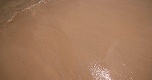 Close-up video of the breathtaking beauty of a sandy beach in Southeast Asia, where the gentle waves of the ocean tenderly embrace the shore with rhythmic grace.  Each wave caresses the golden sand