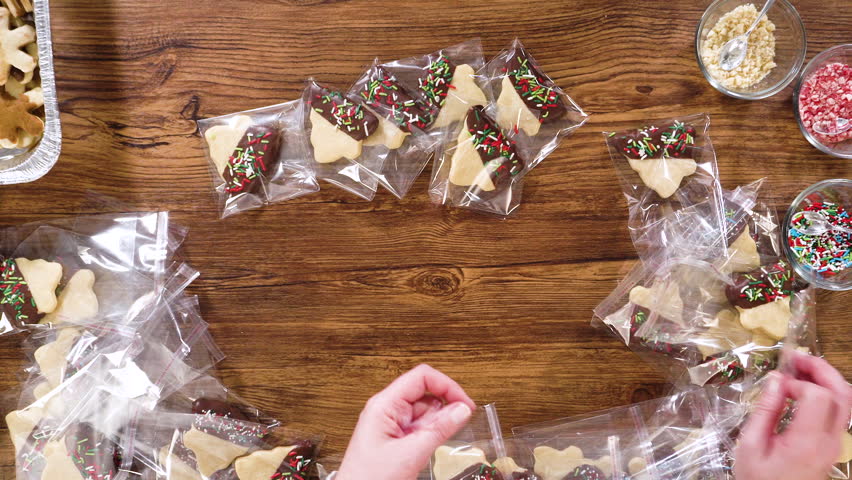 Flat lay. Carefully packaging Christmas cutout cookies, half-dipped in chocolate and presented in clear cellophane wrapping, perfect for festive gifting.