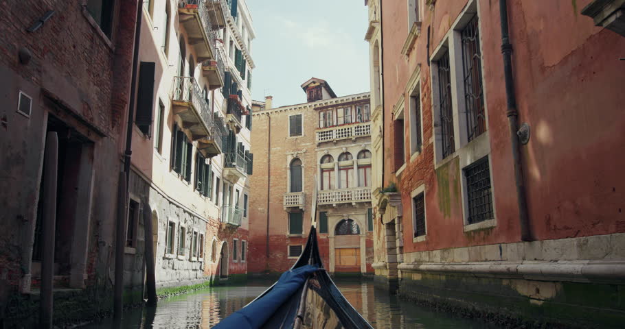 View from a gondola floating on the canals of Venice, Italy. The boat sails through the streets of a romantic city with beautiful architecture in the urban landscape of the Mediterranean. 