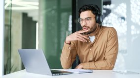 Businessman in wireless headphones watching video call online conference taking notes looking at laptop computer screen sitting in office. Worker listening remote business training talking with tutor - Powered by Shutterstock - Get 15% off with code: PIKWIZARD15