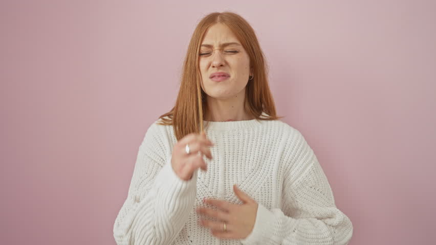 Unwell young redhead wearing sweater coughing furiously, indicative of cold or bronchitis. health care alert over isolated pink background