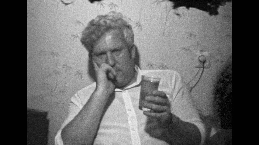Film archive Man holding glass with alcoholic drink, toast, close up. Tired drunk man looking at camera, raising beverage. Adult sad person celebrating weekend indoors. Vintage black white retro 1980s