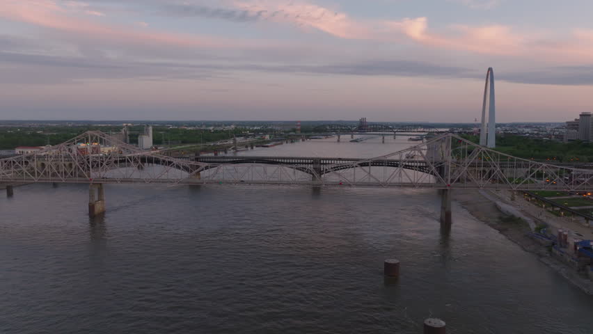 Aerial view of bridges over Mississippi River in St. Louis at dusk, with soft evening sunlight and a city skyline in the background. Urban, transportation, and travel concept