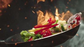 Closeup of chef preparing and throwing vegetable mix on frying pan on fire. Preparation fresh appetizing food. Vegetables flying into the pan in slow motion. Healthy vegetarian food cooking close-up - Powered by Shutterstock - Get 15% off with code: PIKWIZARD15