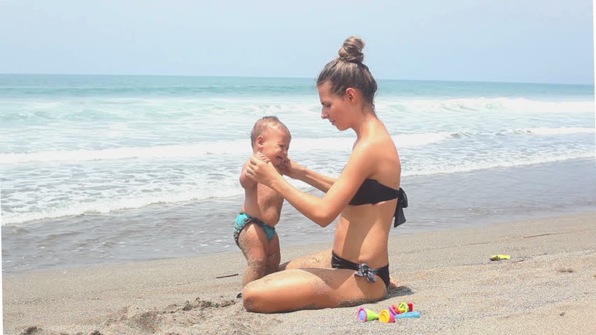 Pretty mother holding her daughter on hands at beach