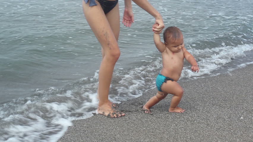 Woman holding by hand her daughter and walking on beach
