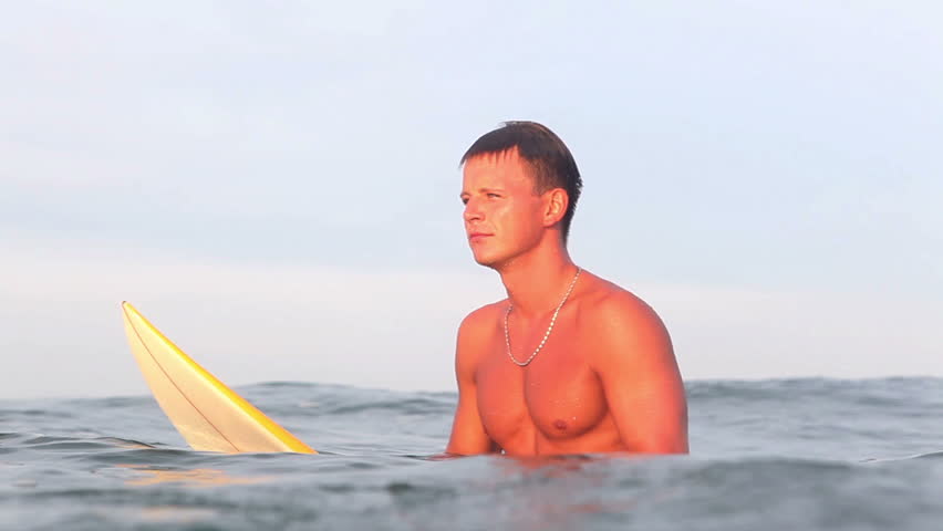Handsome professional surfer sit on surf board and drifting