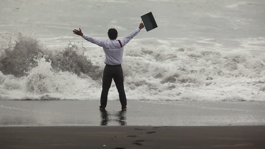 Happy businessman raising hands while big wave comes in to shore