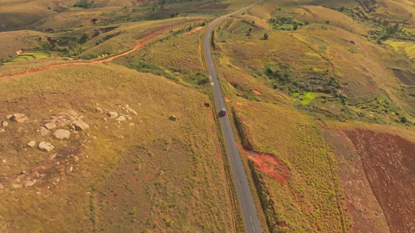 Aerial drone view of van car driving on asphalt road in Madagascar countryside on sunny day. Adventure trip in rural country. Panoramic view. (4K)
