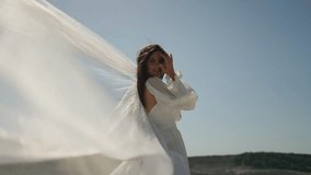 Woman in white dress stands against sky and her veil is blown by wind. Wedding day concept. - Powered by Shutterstock - Get 15% off with code: PIKWIZARD15