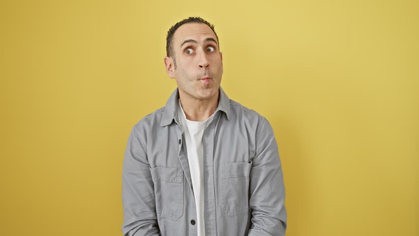 Cute young hispanic guy in shirt making a zany fish face with lips, stands over fun yellow cutout. a comical, crazy expression for a silly, happy portrait.