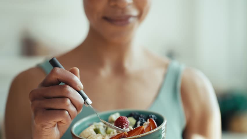 Video of close up of athletic woman eating a healthy fruit bowl in the kitchen at home