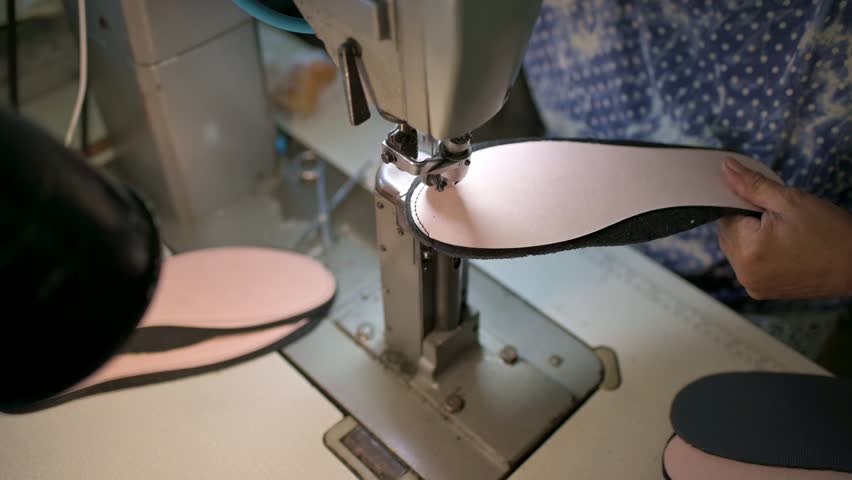 Male shoemaker works on sewing machine at the private workshop. Male bootmaker is sewing fabrics for shoes in shoe workshop. Shoe making process