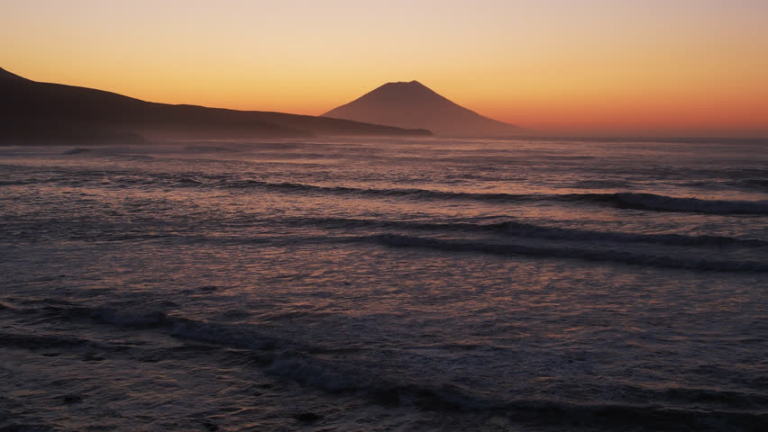 Sunset over ocean waves and dormant volcano . Aerial sun set above mountain silhouette. Abandoned lighthouse nobody nature seascape. North Kuril islands. Cinematic drone. Travel, tourism, mountain
