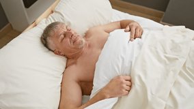 Senior man stretching and yawning while waking up in a bedroom, portraying a refreshed morning routine at home. - Powered by Shutterstock - Get 15% off with code: PIKWIZARD15