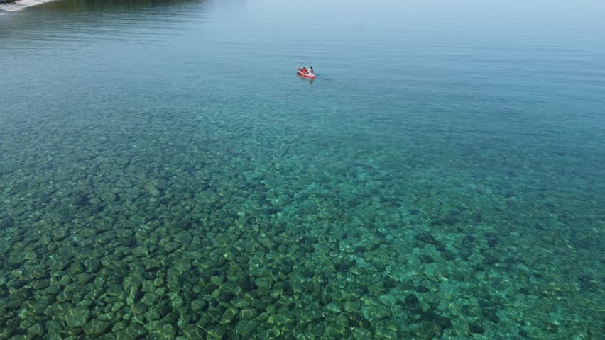 A lone canoer paddles through clear turquoise waters, seen from above. The tranquil and serene scene highlights the beauty and clarity of the lake, perfect for a peaceful outdoor adventure.